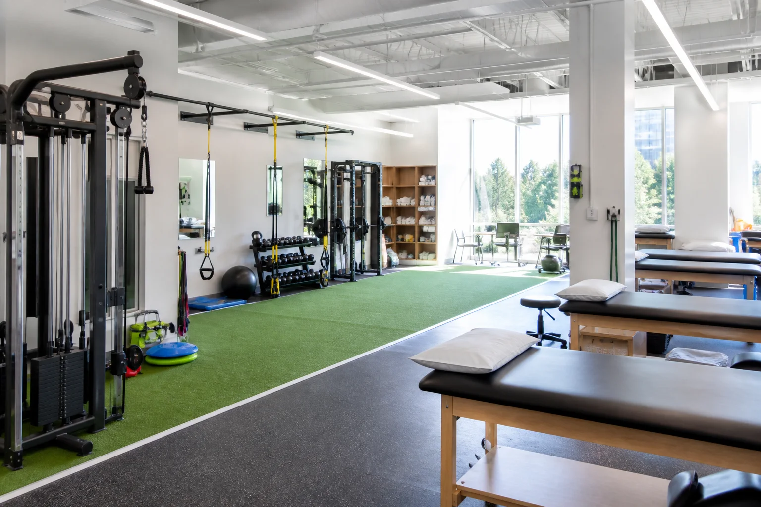 Modern sports rehabilitation facility with turf, cable equipment, and treatment tables