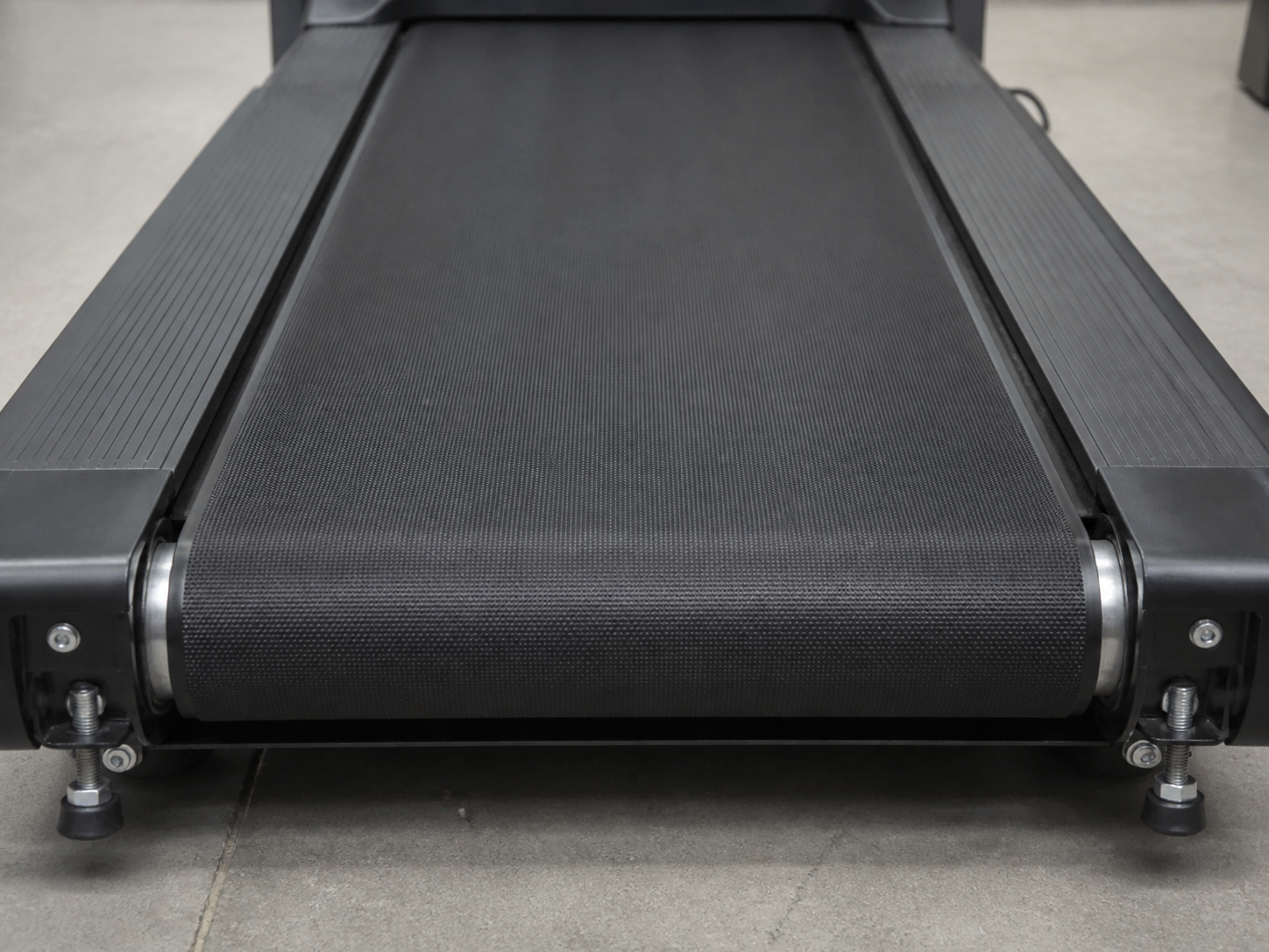 Close-up of a treadmill walking belt and rear roller adjustment hardware